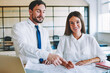 © BullRun - Portrait of successful male and female architects working together on sketches for startup project, smiling woman looking at camera sitting with blueprints in office while man near explaining job