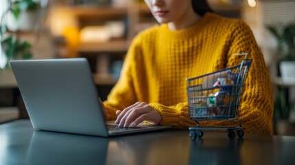 Wall Mural - a woman in a yellow sweater uses a laptop, with a shopping cart nearby, suggesting online shopping o