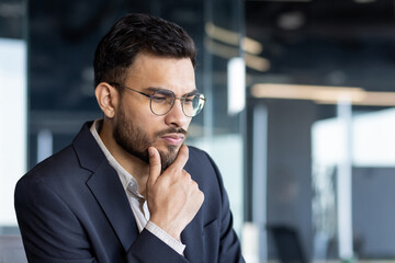 Wall Mural - A thoughtful businessman in a suit, deep in contemplation, reflects serious decision-making in a modern office setting. This image captures professional focus and critical thinking.