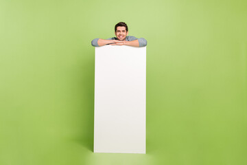 Poster - Full body photo of cheerful young man stand behind long white placard advert isolated on green color background
