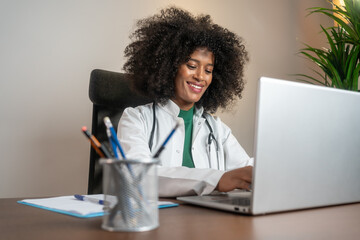 Beautiful smiling female doctor with laptop working at the office desk. Female doctor typing on her laptop computer in medical office.