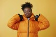 © Markus Schröder - Portrait of a glad afro-american woman in her 40s donning a durable down jacket on pastel yellow background