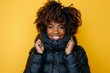 © Markus Schröder - Portrait of a glad afro-american woman in her 40s donning a durable down jacket on pastel yellow background