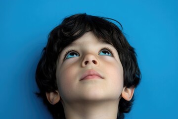 Fototapete - A young boy looks up with bright blue eyes