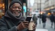 © Centric  - Elderly african american man is smiling while using mobile phone and drinking takeaway coffee outdoors in urban environment