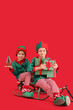 © Pixel-Shot - Cute little boys in elf costumes with Christmas presents and sledge on red background