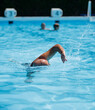 © otterspeer.com Stock - Bald man swims freestyle in a clear, blue pool.  Water splashes visible.  Sunny day.