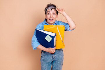 Wall Mural - Charming senior woman holding colorful folders with a cheerful expression on beige background