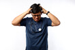 © ArvStd - Young asian man wearing doctor uniform and stethoscope suffering from headache desperate and stressed because pain and migraine. hands on head.