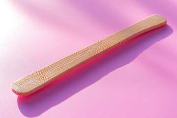 Poster - A small wooden toothbrush lying on a pink surface, ideal for illustration or design