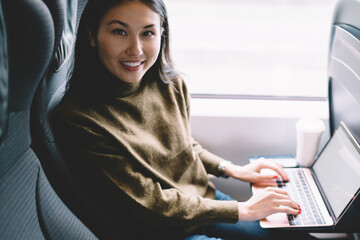 Wall Mural - Portrait of cheerful asian female enjoying transportation via train with laptop computer learn course remotely, attractive woman blogger working online during journey using laptop computer in wagon