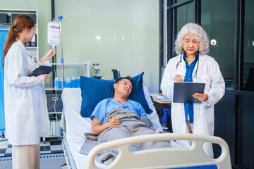 Wall Mural - Two female doctors examine a patient lying on a hospital bed,discuss the medical chart,administer medicine,and provide encouragement, ensuring compassionate care and fostering the patient's recovery