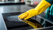 © mahamad - A housewife using protective gear to clean and polish a shiny black electric cooker in her kitchen.