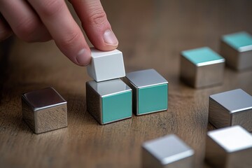 Poster - A hand stacking cubes with a mix of metallic and colored surfaces on a wooden table.