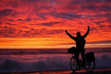 Poster - A silhouetted cyclist celebrates against a vibrant sunset over the ocean waves.