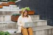 © mdyn - Happy 30 blonde woman sitting on the stairs and working on laptop, fast connection. A beautiful girl with a laptop is sitting on the street. freelancer. Work remotely