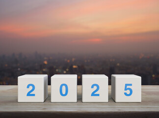 Wall Mural - 2025 letter on white block cubes on wooden table over blur of cityscape on warm light sundown, Happy new year 2025 cover concept