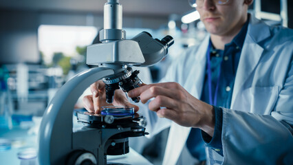 Leinwandbilder - Close Up Portrait of a Young Microbiologist Wearing Glasses and Looking Through the Microscope, Analyzing Sample Cells. Cheerful Scientist Working in a Medical Science Laboratory