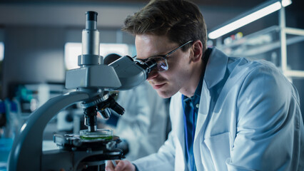Leinwandbilder - Portrait of a Handsome Caucasian Student Working on a Research Project in University. Medical Research Scientist Looking at Biological Samples Under a Microscope in an Applied Science Laboratory