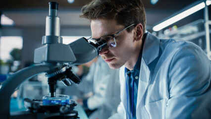 Leinwandbilder - Portrait of a Young Smart Scientist Working in a Laboratory, Using Advanced Microscope, Writing Down Research Data in a Paper Notebook. Caucasian Biotechnology Specialist Using Modern Tools