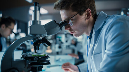 Leinwandbilder - Portrait of a Young Smart Scientist Working in a Laboratory, Using Advanced Microscope, Writing Down Research Data in a Paper Notebook. Caucasian Biotechnology Specialist Using Modern Tools