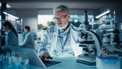 Wall Mural - Portrait of a Middle Aged Scientist Working in a Laboratory, Using Laptop Computer, Writing Down Research Data in a Paper Notebook. Caucasian Biotechnology Specialist Using Modern Tools