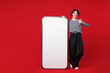 © ViDi Studio - Full body young happy woman in blue striped sweatshirt casual clothes big huge blank screen mobile cell phone smartphone with workspace copy space area show thumb up isolated on plain red background