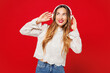 © ViDi Studio - Young smiling happy Caucasian woman she wear white blouse casual clothes listen to music in headphones look aside on area mock up isolated on plain red background studio portrait. Lifestyle concept.