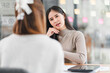 © kenchiro168 - young woman in beige sweater attentively listens during conversation at table, with tablet placed nearby, in modern indoor