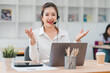 © kenchiro168 - cheerful woman wearing headset is working on laptop in modern office, engaging in video call or customer service interaction. coffee cup and office supplies are on desk