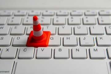 A miniature traffic cone placed on a computer keyboard. Website maintenance, technical difficulties, website under construction concept.