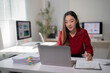© Tj - Young businesswoman wearing a red shirt, working on a laptop while analyzing financial documents, charts, and graphs in a modern office environment