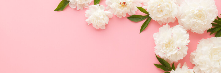 Wall Mural - Fresh beautiful soft white peony flowers with green leaves on light pink table background. Pastel color. Closeup. Empty place for inspirational text, quote or sayings. Wide banner. Top down view.
