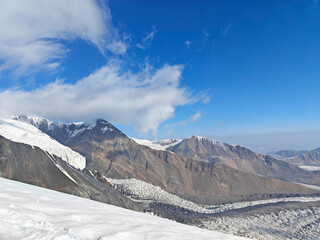 Wall Mural - Snow blankets the rugged mountains as clouds drift across a vibrant blue sky in a pristine landscape