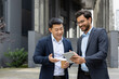 © Liubomir - Two professional men in suits having a discussion over a tablet outdoors. One is holding a coffee cup, and both are smiling, signifying a positive and collaborative business interaction.