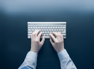 Aufkleber - Overhead view of gloved hands typing on a wireless keyboard, positioned on a dark surface.  Clean, sterile, and focused on the task at hand.