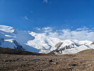 Wall Mural - Snow blankets the mountain peaks with a backdrop of bright blue skies and scattered clouds in the distance