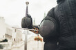 © Soloviova Liudmyla - Long medieval sharp sword and protective mask close-up and warrior dressed in black historical fencing armor. Historical items and old traditions and battle restorations, sporty people concept.