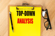 © Iryna - Top-down analysis concept with yellow clipboard, black pen, and eyeglasses on wooden desk
