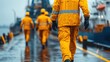 © kwangze - Workers in yellow rain gear walk along a wet dock, emphasizing their role in maritime labor and safety in challenging weather conditions.