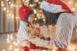 © oatawa - Asian mother and baby in santa celebrate Christmas. New Year's holidays. Toddler with mom in the festively decorated room.