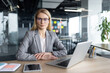 © Liubomir - A professional businesswoman sits confidently at her desk in a modern office setting, equipped with a laptop and smartphone, reflecting a blend of technology and professionalism.