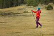 © VICTOR - A woman in a red jacket and blue hat is walking in a field with a pair of poles
