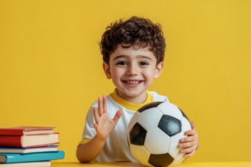 Poster - A cheerful boy holding a soccer ball with books beside him against a yellow background.