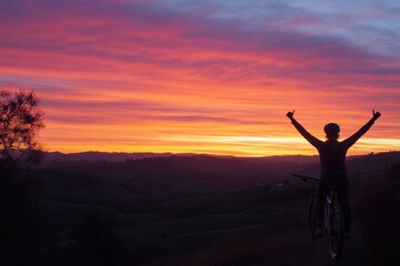Poster - Silhouette of a cyclist celebrating at sunset, surrounded by scenic hills and vibrant colors.