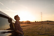 © kieferpix - Carefree man traveler next to car watching the sunset looking up to the sky feeling happy and at peace in nature