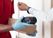 © Prostock-studio - Modern payment technologies and self isolation. Close up shot of young black woman paying for order with smartwatch, taking box from courier in protective gloves, covid-19 preventive measures concept