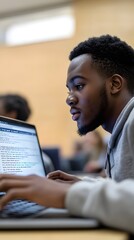 Aufkleber - A young man focused on coding or studying on a laptop in a classroom setting.