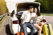 © Prostock-studio - Young affectionate couple traveling by auto, sitting in car trunk with suitcase and guitar, holding map, checking destination. Millennial woman and her boyfriend having road trip on summer vacation