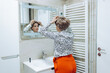 © Milos - In a well-designed bathroom, a person suffering from cancer is seen adjusting their hairpiece, reflecting personal transformation and the journey of self-identity in a modern space.